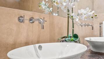 Un baño con una bañera independiente, un espejo y orquídeas blancas.