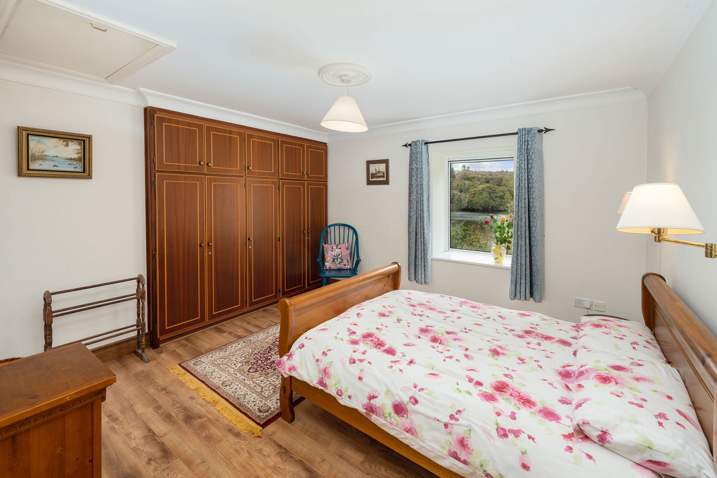 A bedroom with a wooden bed, a wardrobe, a chair, and a window with curtains.