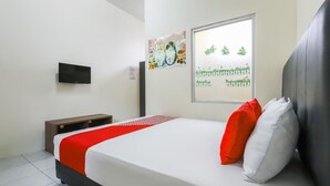 A neatly made bed with a white and red bedspread, a black headboard, and two pillows, one red and one white. A flat-screen TV is mounted on the wall, and a window with a view of greenery is visible. - OYO 3830 Dfarys Gh Syariah (Balikpapan)