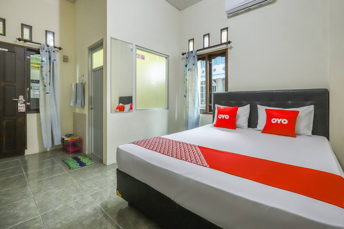 A hotel room with a bed, a mirror, a window, and a door.
