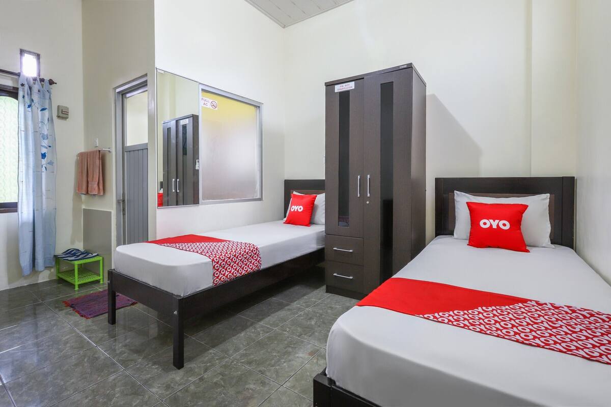 A hotel room with two beds, a wardrobe, a mirror, and a small green stool.