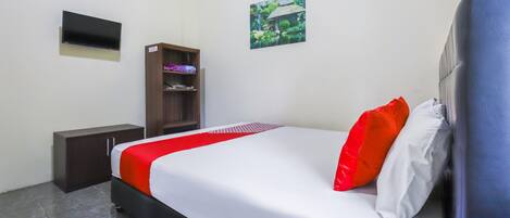 A hotel room with a bed, a TV mounted on the wall, a small cabinet, and a picture of a house.