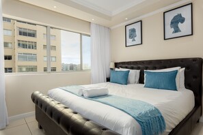 Ein modernes Hotelzimmer mit einem großen Bett, Blick auf die Stadt und gerahmten Kunstwerken an der Wand.