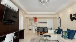 A modern living room with a flat-screen TV, a glass coffee table, a sofa with colorful pillows, and a dining area with chairs and a red accent wall. - New Cumberland 405 (Cape Town)