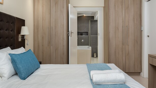 A hotel room with a large bed, a wardrobe, a bathroom, and a nightstand. - New Cumberland 405 (Cape Town)