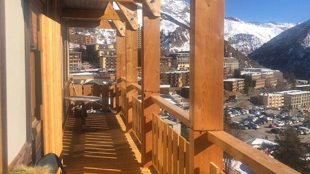 A wooden balcony with a view of a snow-covered mountain and a town below. - Logement 6 Pers sur les Pistes de Skis vue Panoramique (Orcieres)