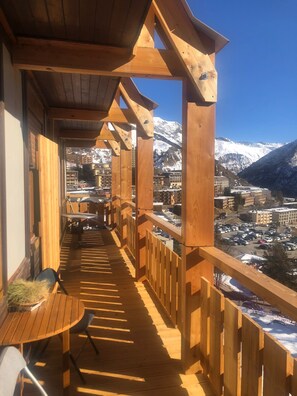 A wooden balcony with a view of a snow-covered mountain and a town below.