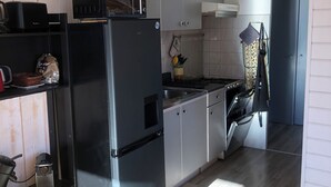 A modern kitchen with a black refrigerator, a stove, and a microwave. There is a wooden cabinet and a hanging pot rack. - Logement 6 Pers sur les Pistes de Skis vue Panoramique (Orcieres)