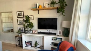 Olohuone, jossa on sininen nojatuoli, televisio, kirjahylly ja ikkuna, jossa on verhot.