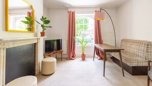 Ett vardagsrum med en öppen spis, en tv, en soffa och krukväxter.