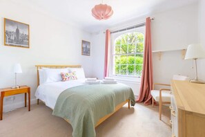 A bedroom with a bed, bedside table, lamp, window with curtains, and a desk with a chair. - Charming & Central 2BD Flat - Islington (London)