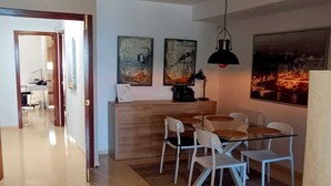 En moderne stue med en brun sofa, et spiseområde med hvide stole og et køkken i baggrunden.