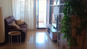 En stue med sofa, et lille bord, et TV-møbel og en potteplante.