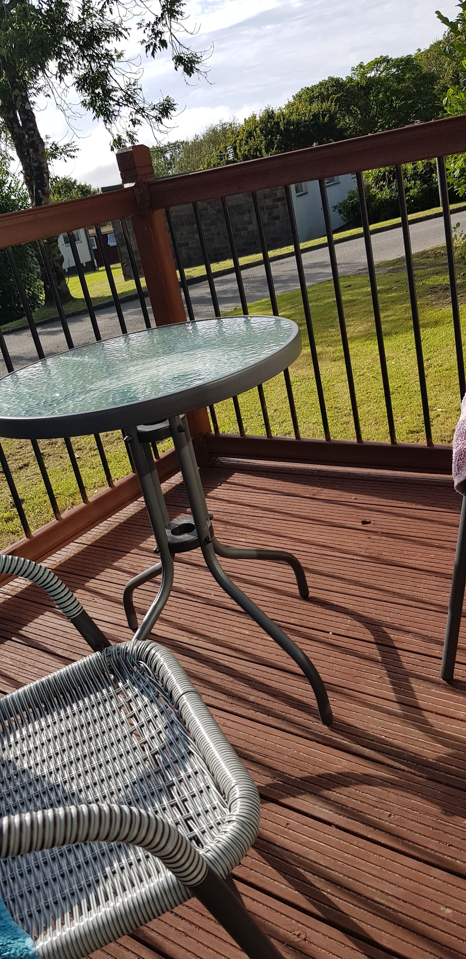 Una terraza de madera con una mesa de vidrio y sillas de mimbre.