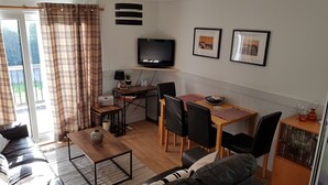A compact living space with a dining area, a sofa, a TV, and a small table with chairs.