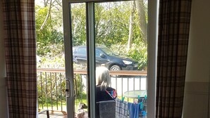 A living room with a sofa, a table, a ceiling light, a sliding glass door leading to an outdoor area with a car and a dog.