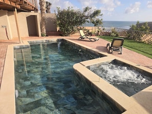 A clear swimming pool with a waterfall feature, surrounded by a patio with chairs and a view of the ocean. - Villa: Oceanfront, 6 Beds, Pool & Beach Access (Mirleft)
