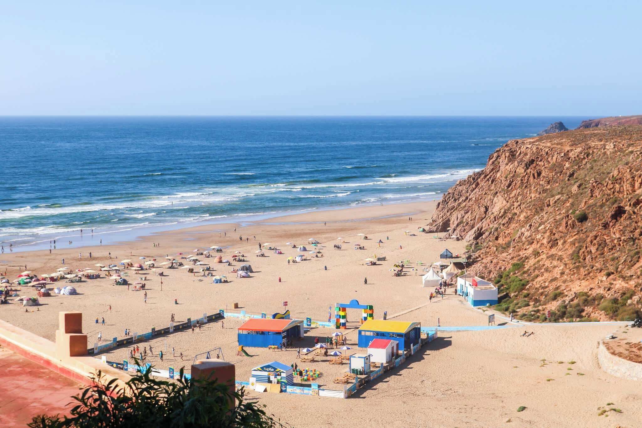A beach with tents and beach huts, a clear sky, and the ocean.