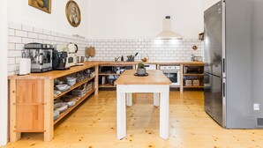 A kitchen with white tiled walls, wooden flooring, a stainless steel refrigerator, a wooden table, and various kitchen appliances. - Soví dom flat 1 (Svätý Anton)