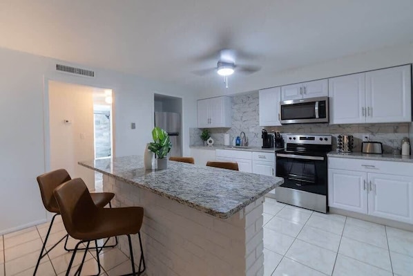 A modern kitchen with white cabinets, a granite countertop, a stainless steel oven, and a microwave. - Beach getaway w/ pool near Kennedy Space Center (Cape Canaveral)