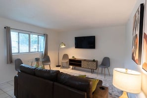 Un salon moderne avec un canapé en cuir, une petite table ronde, un téléviseur fixé au mur et un buffet.