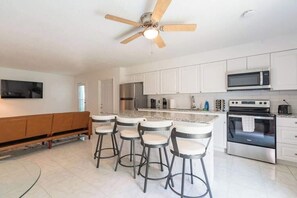 A modern kitchen with white cabinets, a central island with bar stools, a ceiling fan, and stainless steel appliances.