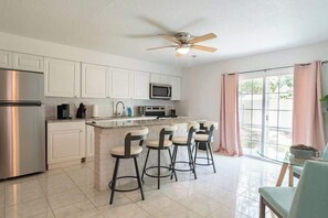 A kitchen with a central island, bar stools, stainless steel appliances, and a ceiling fan.