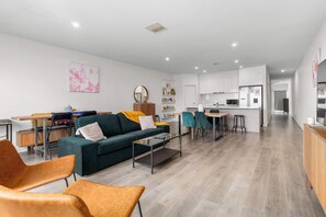 Een moderne woonkamer met een bank, stoelen, een salontafel, en een eethoek met een keuken op de achtergrond.