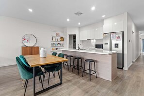 Una cocina moderna con armarios blancos, una isla central con taburetes y un comedor con mesa de madera y sillas verdes.