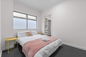 Una habitación de hotel con una cama, una ventana, un armario y una pequeña mesa.
