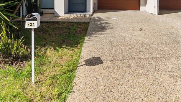 Un immeuble résidentiel moderne à deux étages, doté d’un garage à l’avant, d’une boîte aux lettres et d’un petit jardin.