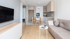 Una sala de estar moderna con un televisor de pantalla plana, un sofá, una mesa de comedor con sillas y una zona de cocina con armarios y un refrigerador.
