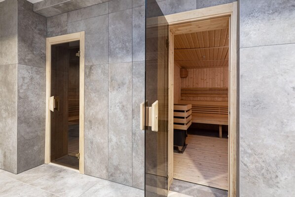 Eine Sauna mit Holzvertäfelung und Glastür vor einer grauen, mit Fliesen verkleideten Wand.