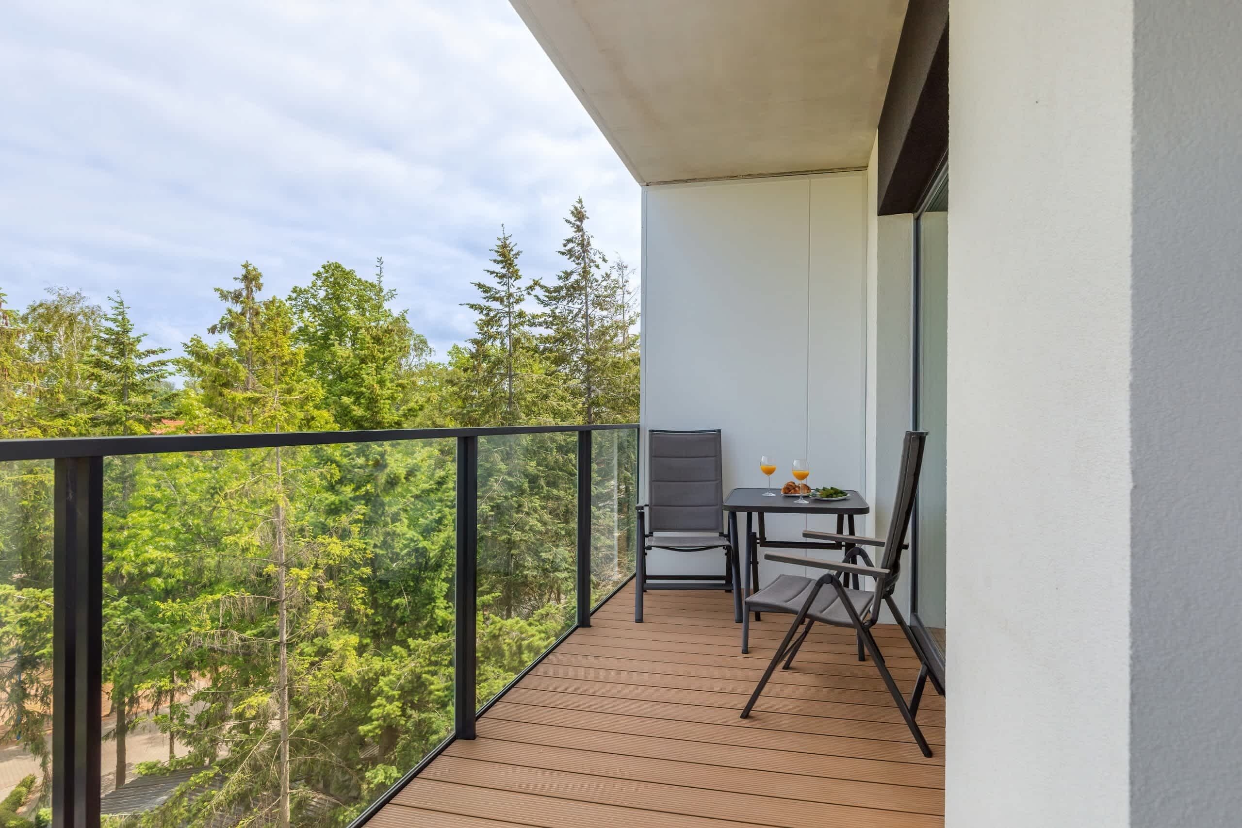 Un balcon doté d’un plancher en bois, d’une table avec deux chaises et d’une rambarde en verre.