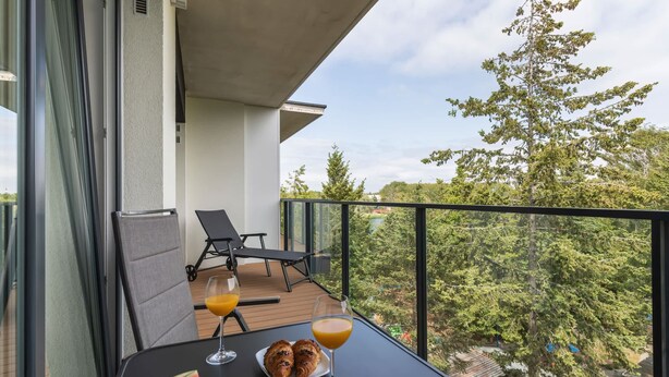 Un balcon avec une table dressée pour le petit-déjeuner, comprenant des croissants et un verre de jus d’orange, donnant sur un paysage verdoyant et luxuriant.