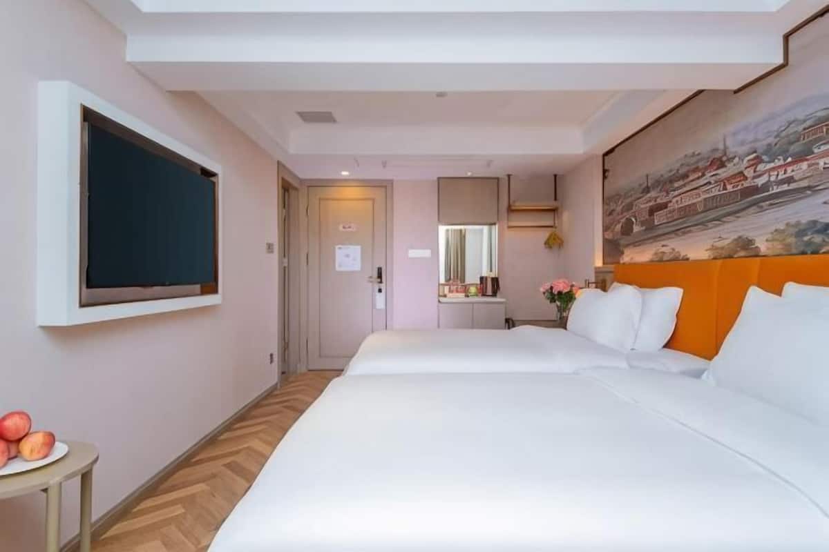 A hotel room with a bed, a small table with fruit, a painting on the wall, and a door leading to another room.