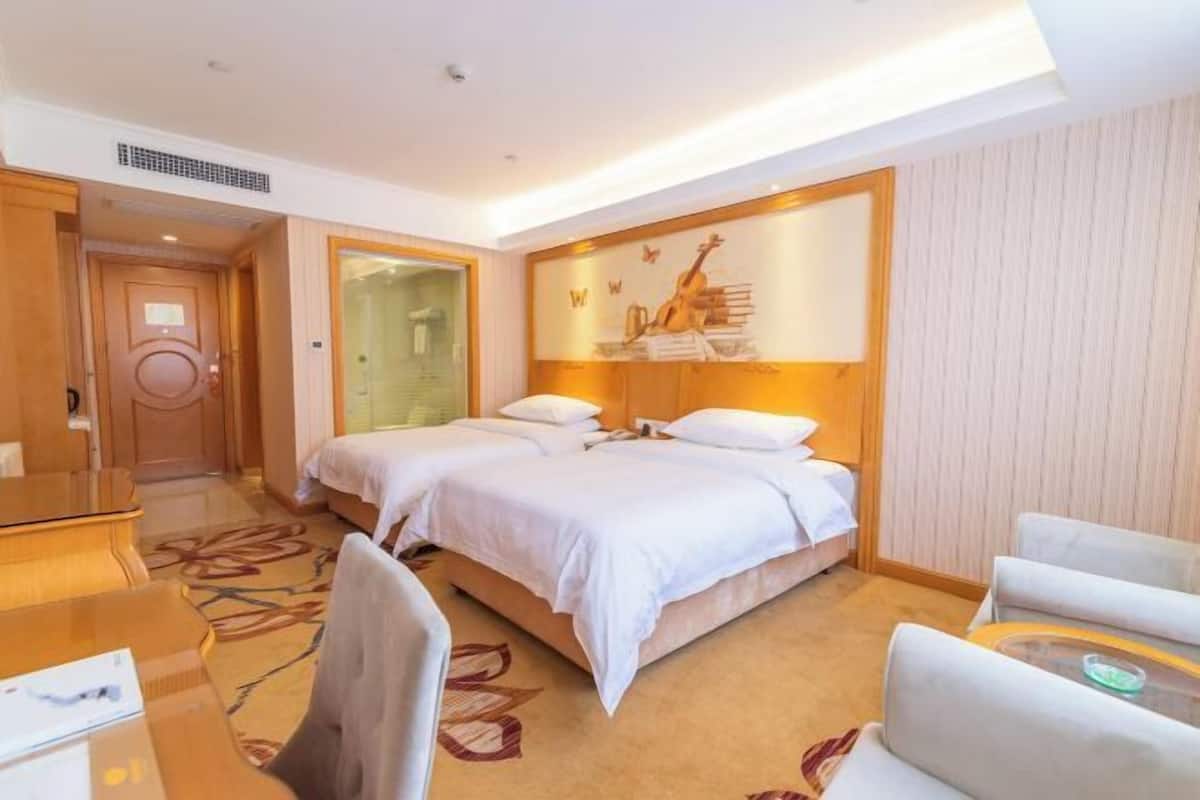 A hotel room with a bed, a desk, a chair, and a wall-mounted artwork.
