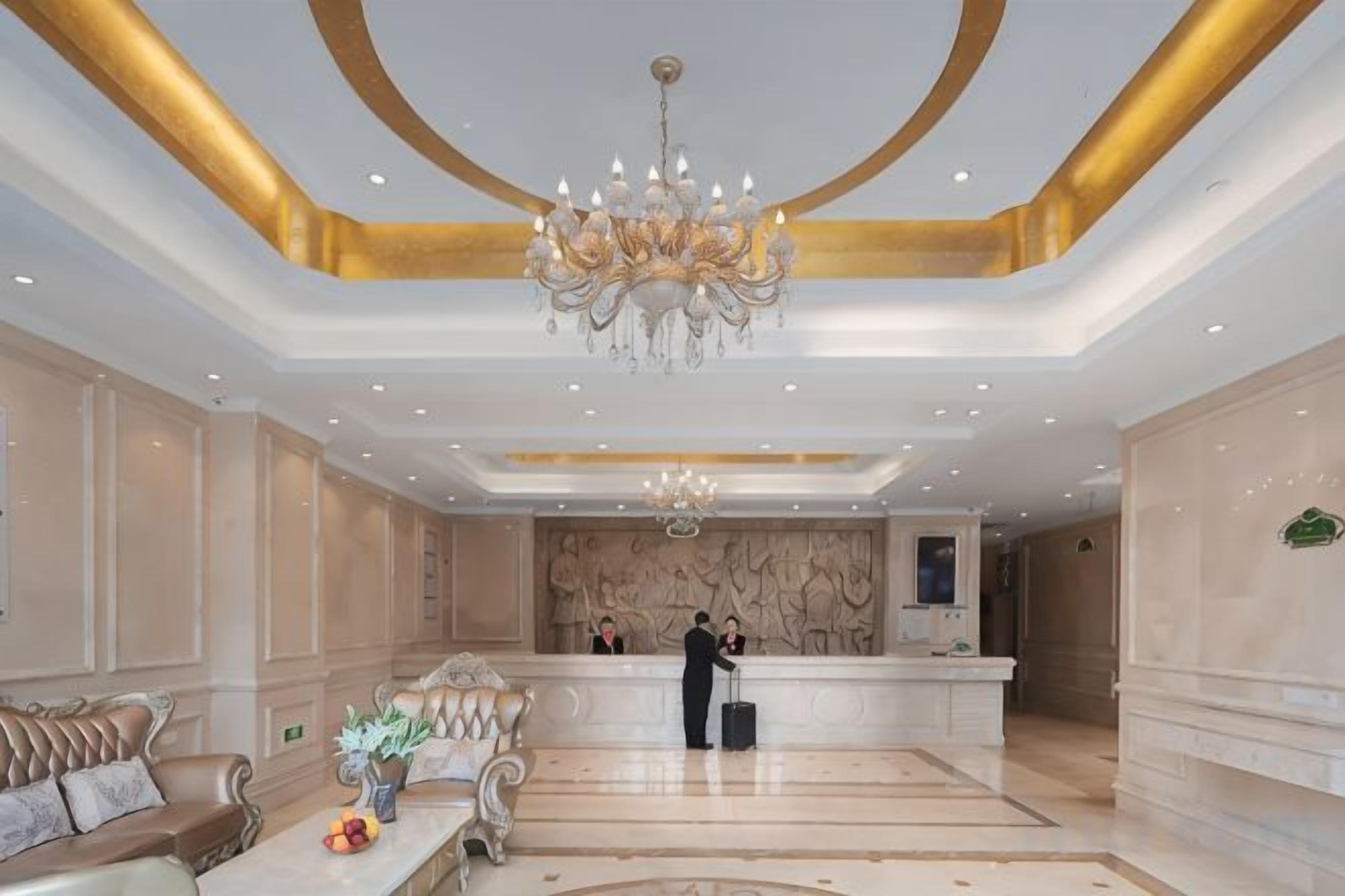 Vestíbulo de hotel con mostrador de recepción, zona de estar y candelabro.