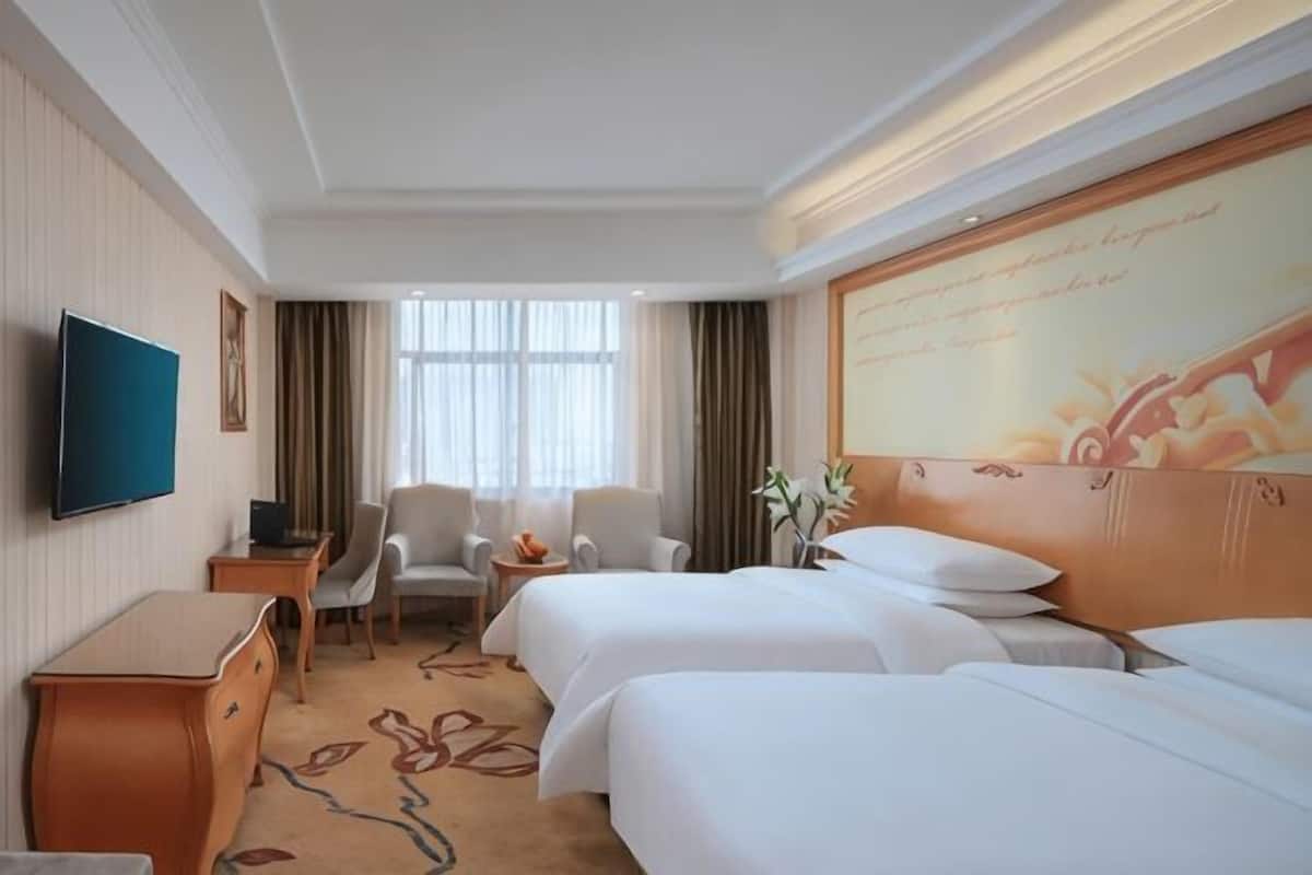 A hotel room with two beds, a TV, a desk, and a chair.