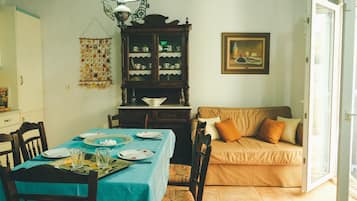 A dining area with a table set for two, a cabinet with dishes, a sofa, and a painting on the wall.