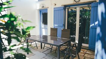 A patio with a table and chairs, a blue door, and a window with a view of greenery.