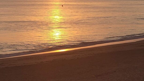 A sunset over a calm sea with a beach in the foreground.