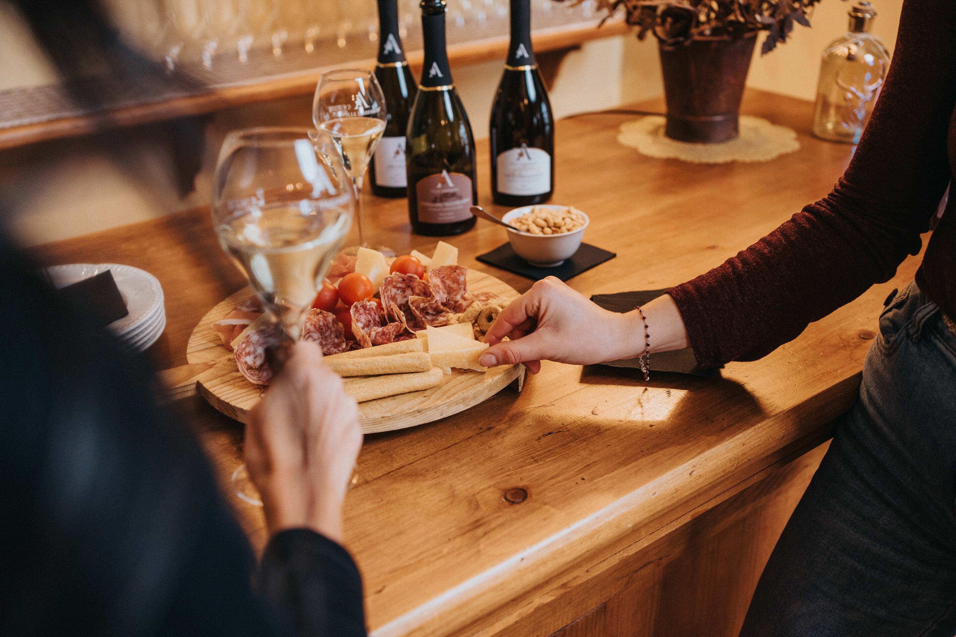 Una mesa de madera con una tabla de embutidos, botellas de vino y copas.