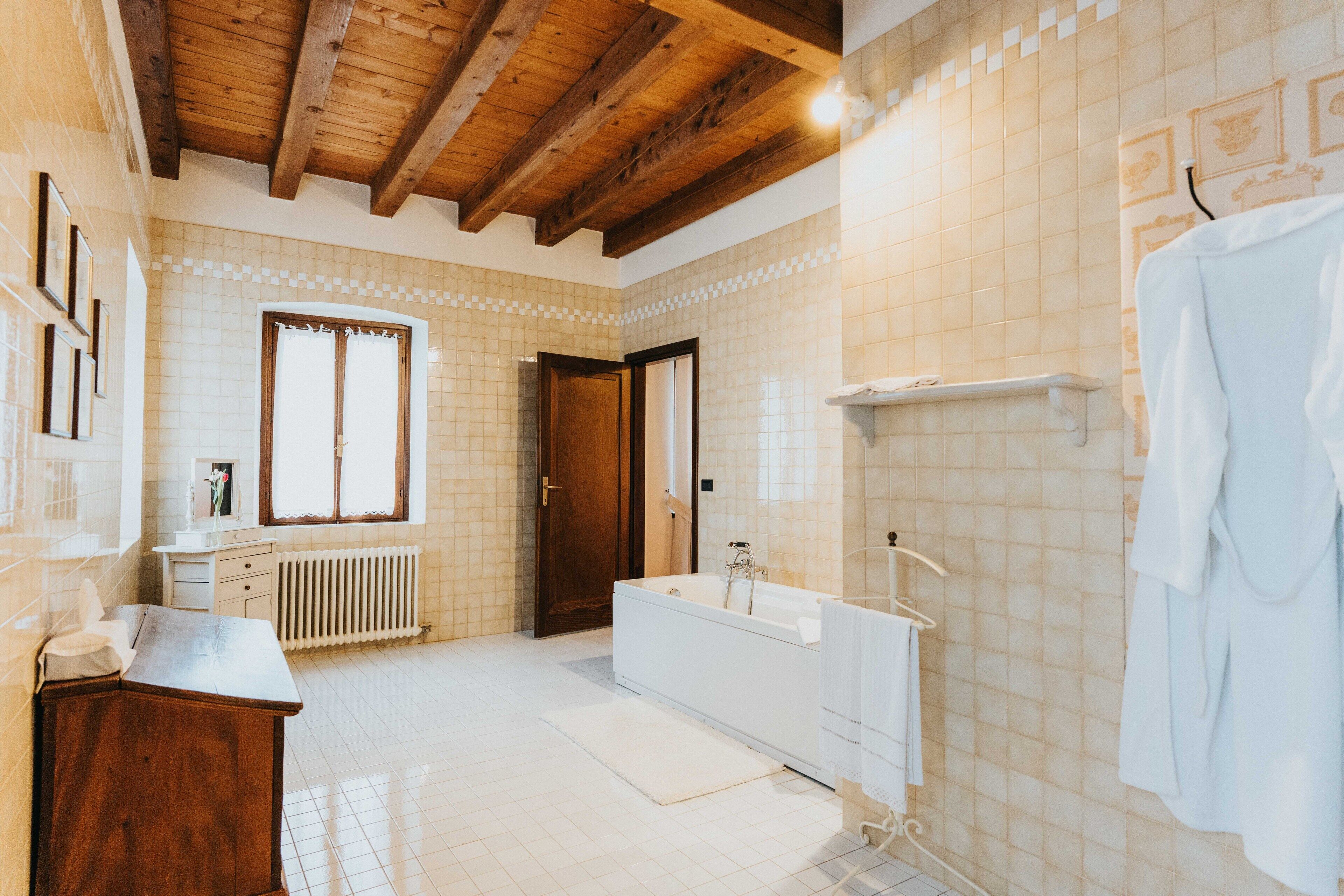 A spacious bathroom with a wooden ceiling, a bathtub, a white sink, and a towel rack.