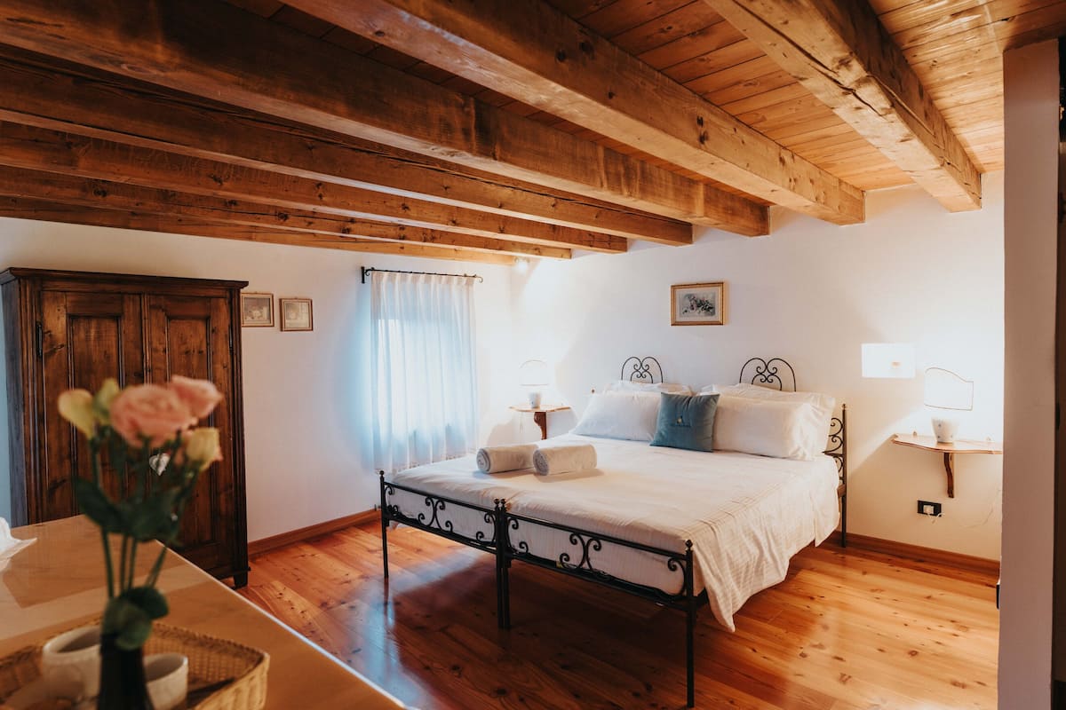 Un dormitorio con techo de madera, una cama con ropa blanca, una mesita de noche con lámpara y un armario de madera.