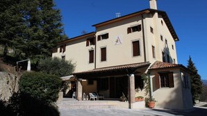 Un edificio de dos plantas con un patio, una estructura pequeña adosada y montañas al fondo.