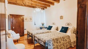 Un dormitorio con dos camas, un armario de madera, un sillón blanco y una araña.