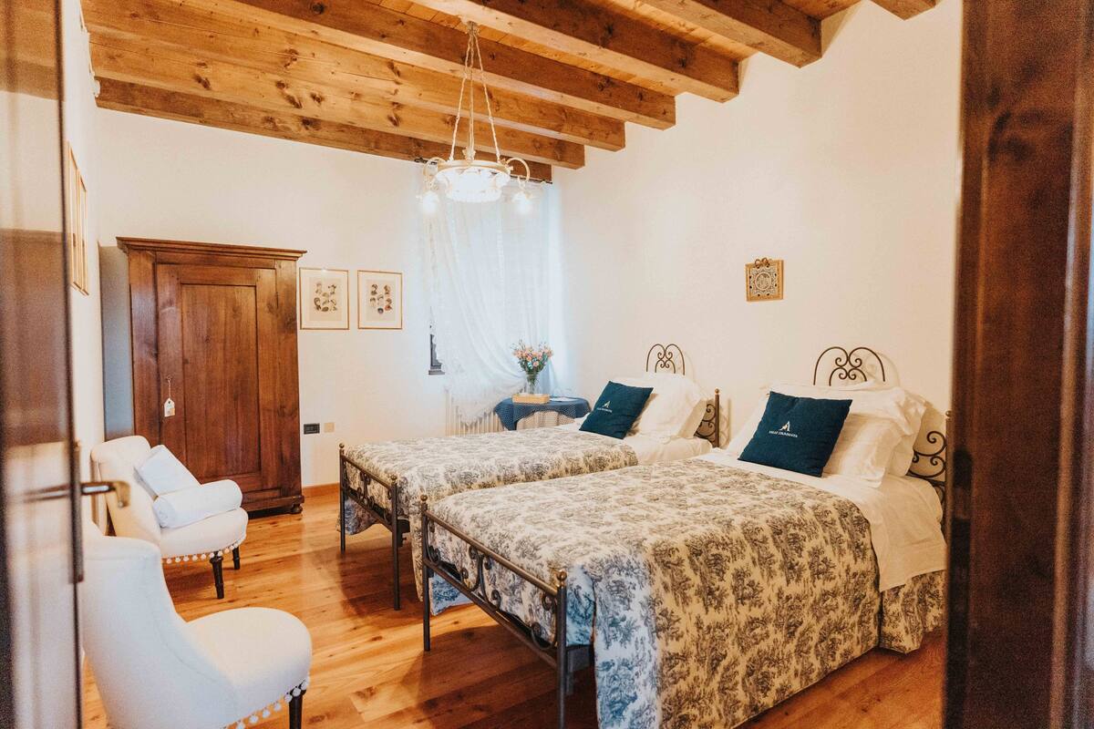Un dormitorio con dos camas, un armario de madera, un sillón blanco y una araña.