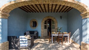 Un patio esterno con tavolo apparecchiato per mangiare, un divano in vimini e una sedia.