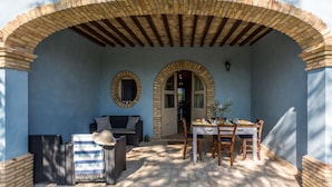 Une terrasse extérieure avec une table dressée pour le repas, un canapé en osier et un fauteuil.